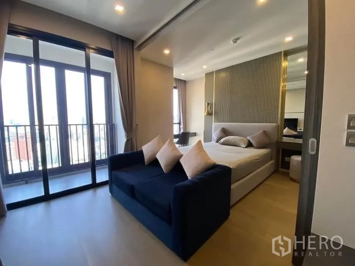 Condominium for rent in Watthana, Bangkok - Bright 1-bedroom condo with sofa, bed, and sliding doors to a balcony overlooking the Bangkok skyline.