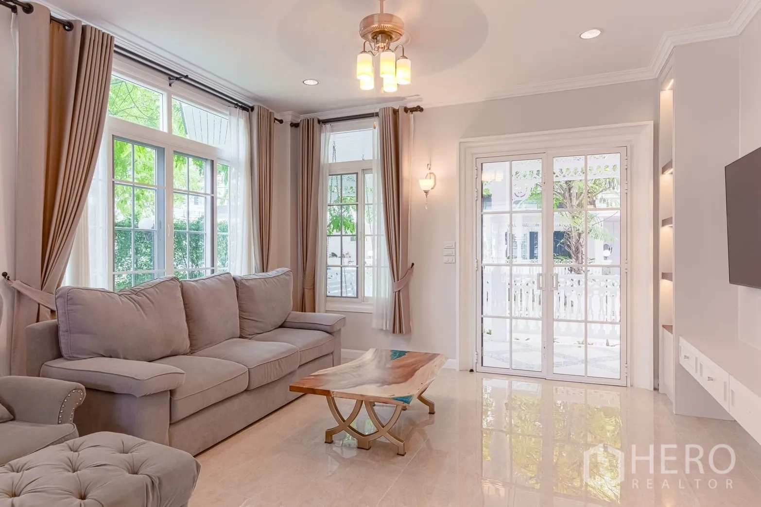 Detached House for rent in Bang Na, Bangkok - Sunlit living room with gray sofa, large curtained windows, and French doors.