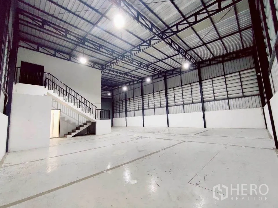 Warehouse for rent in Lam Luk Ka, Pathum Thani - Open warehouse floor with bright coated surface and staircase to office.