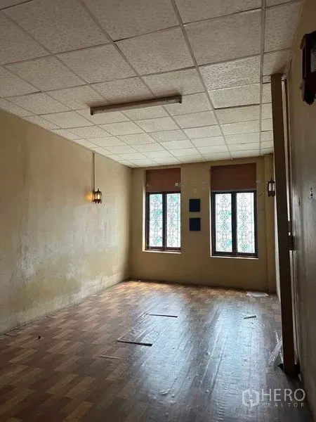 Shophouse for rent in Samphanthawong, Bangkok - Upper-floor room featuring two tall windows, a drop ceiling and aged wooden flooring for office or studio use.