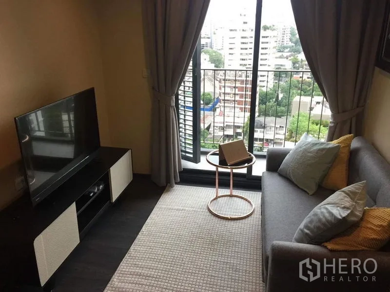 คอนโด ให้เช่าในWatthana, Bangkok - ห้องนั่งเล่นพร้อมชั้นวางทีวีและประตูกระจกบานเลื่อนเปิดสู่ระเบียงวิวชุมชน