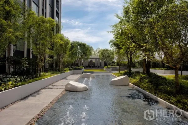 Condominium for rent in Pathum Wan, Bangkok - Serene water feature with stepping stones and small fountains amid lush trees and walkways.