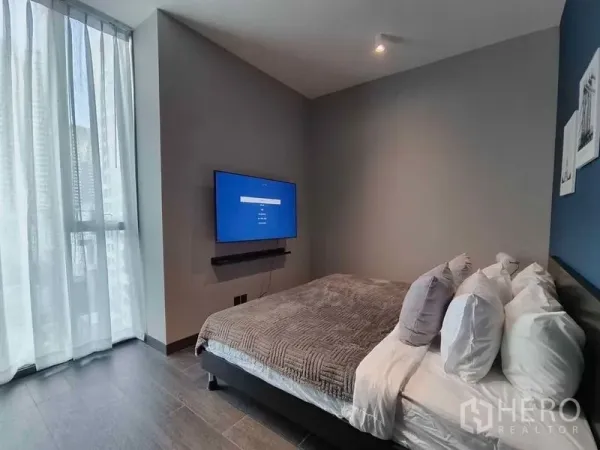 Condominium for rent in Bang Rak, Bangkok - Bedroom with floor-to-ceiling window, wall-mounted TV, and neatly made bed.