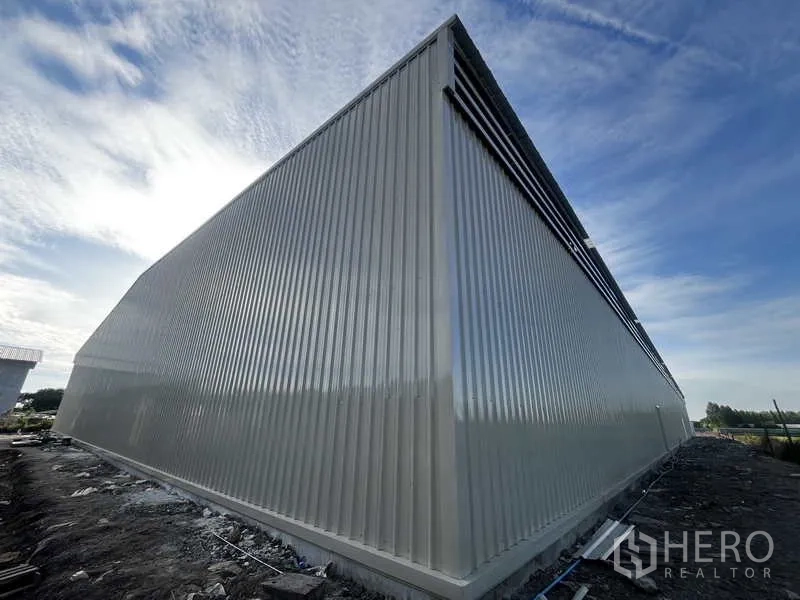 Warehouse for rent or sale in Pak Kret, Nonthaburi - Angled corner view showing ribbed metal wall panels and raised concrete foundation.