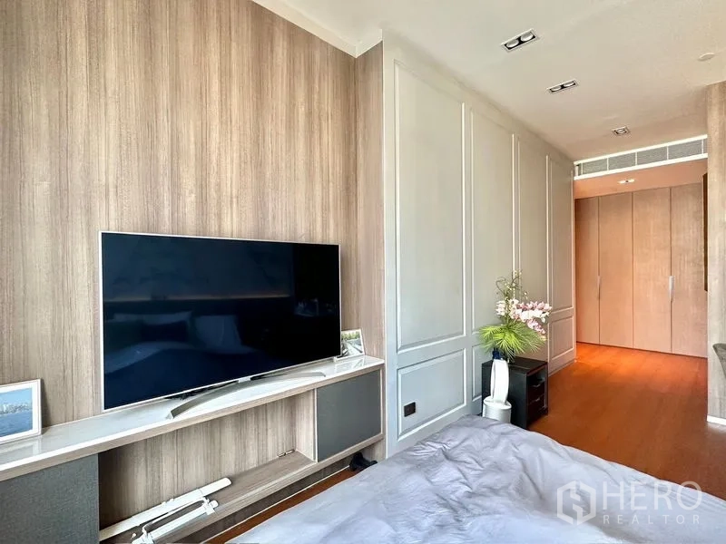 Condominium for rent in Pathum Wan, Bangkok - Bedroom TV wall with wood paneling, storage and walkway to closets.