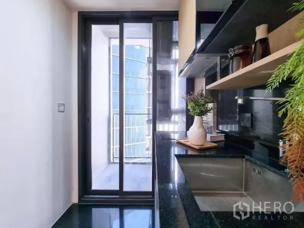 公寓 出售 - 走廊式厨房，黑色石材台面，推拉门通向阳台。