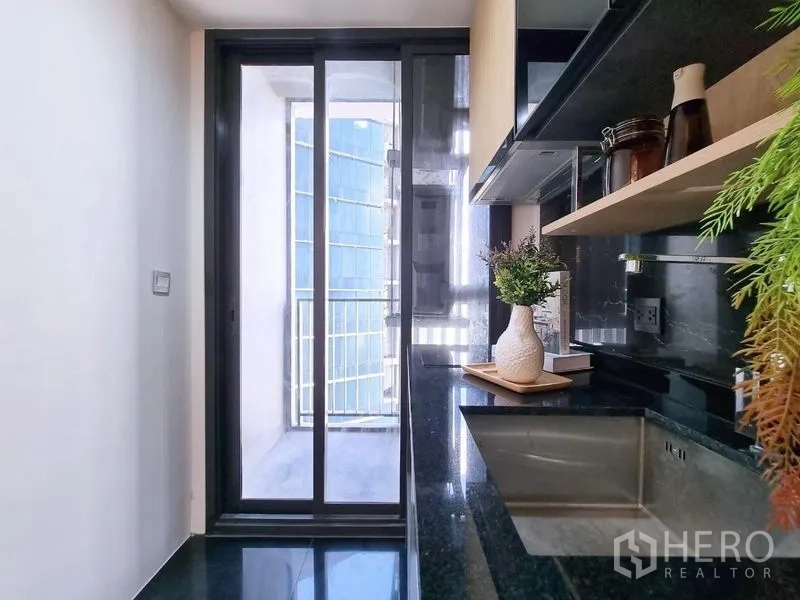 公寓 出售 - 走廊式厨房，黑色石材台面，推拉门通向阳台。