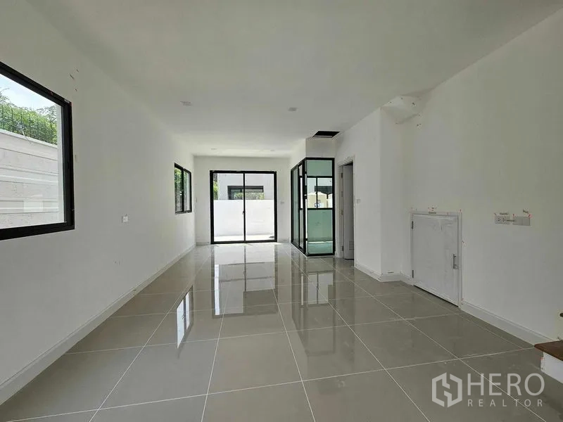 联排别墅 出租在Bang Kapi, Bangkok - 一层开放式客餐厅，亮面瓷砖地、推拉玻璃门与玻璃围合的厨房区。