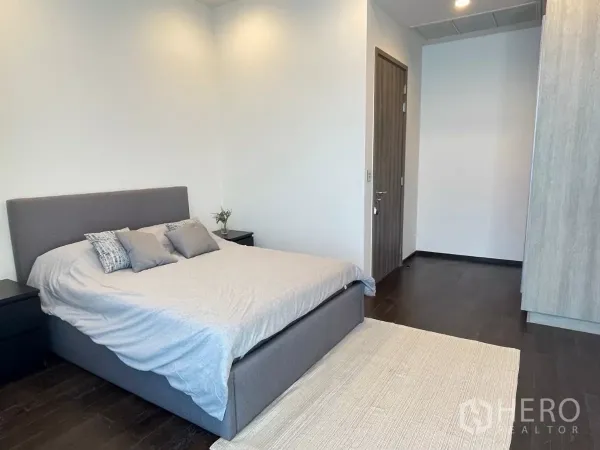 Condominium for rent in Phra Khanong, Bangkok - Minimalist bedroom featuring a gray upholstered bed, side tables and dark wood flooring.