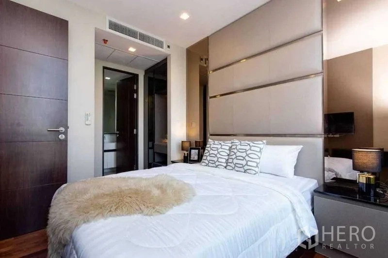 Condominium for sale in Ratchathewi, Bangkok - Bedroom with padded headboard, bedside tables, and a door leading to the bathroom.