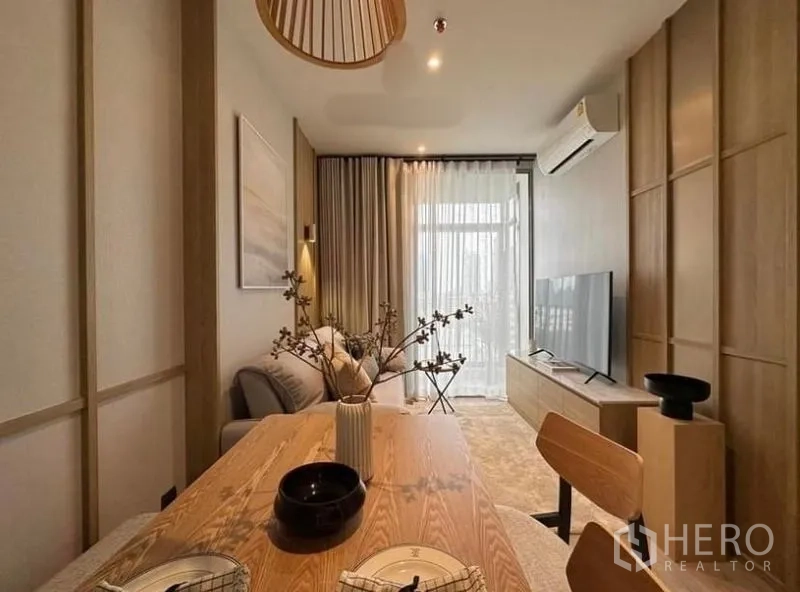 公寓 出租或出售在Watthana, Bangkok - 温暖木质风客餐厅，木桌、沙发、电视柜与空调，落地窗帘连接明亮阳台。