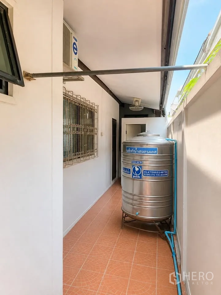 Detached House for rent in Prawet, Bangkok - Side corridor with terracotta tiles, window grilles and stainless water tank.