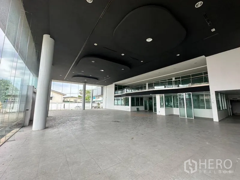 Showroom for rent or sale in Lam Luk Ka, Pathum Thani - Double-height showroom hall with black acoustic ceiling and glass facade.