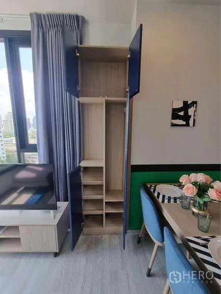 公寓 出租在Watthana, Bangkok - 靠窗的高储物柜打开展示多层搁板，毗邻电视与餐区。