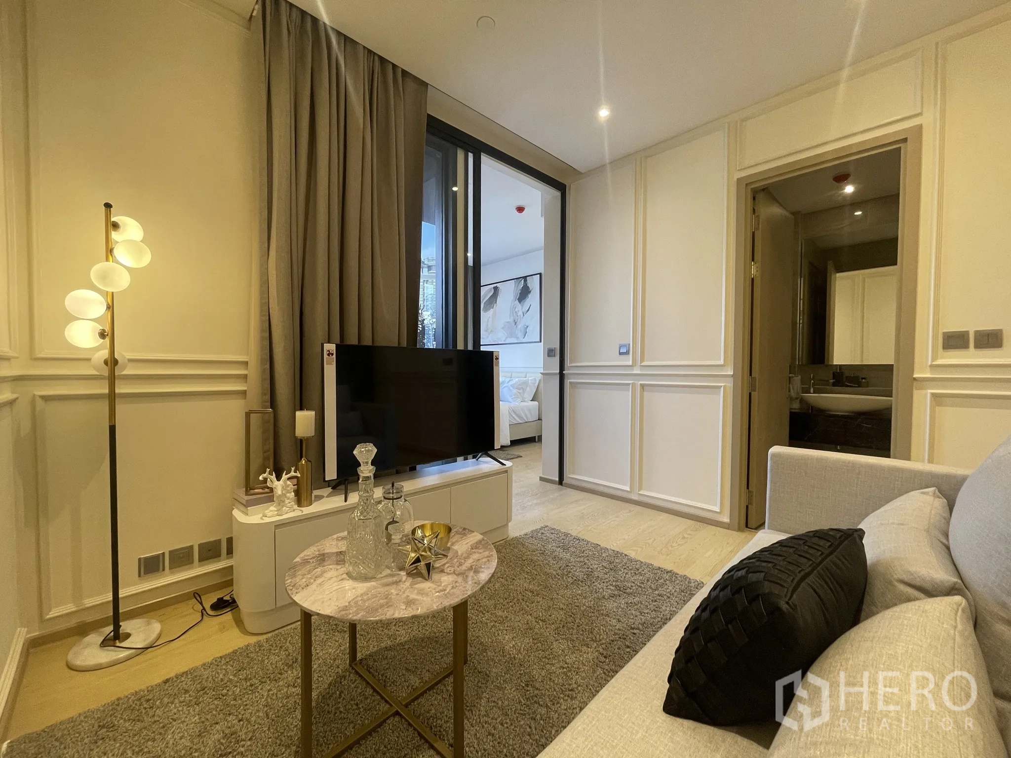 คอนโด ให้เช่าในDin Daeng, Bangkok - มุมห้องนั่งเล่นมองไปยังห้องนอนผ่านประตูบานเลื่อน พร้อมชั้นวางทีวี โคมไฟยืน และประตูห้องน้ำ