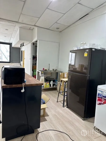 店屋 出租在Khlong Toei, Bangkok - 小厨房一角，冰箱、微波炉、开放式置物架与不锈钢水槽。