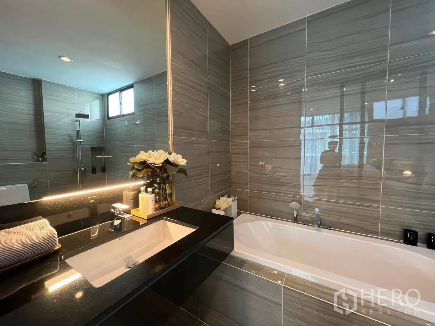 Townhouse for rent in Saphan Sung, Bangkok - Bathroom with black stone vanity, built-in bathtub, and gray tiled walls.