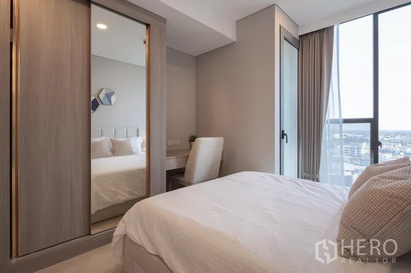 Condominium for rent in Khlong Toei, Bangkok - Second bedroom with sliding mirrored wardrobe, work desk nook, and tall window with city outlook.