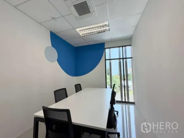 办公空间 出租在Huai Khwang, Bangkok - 带蓝色点缀墙的办公室，长桌与落地窗，可见城市与绿景。