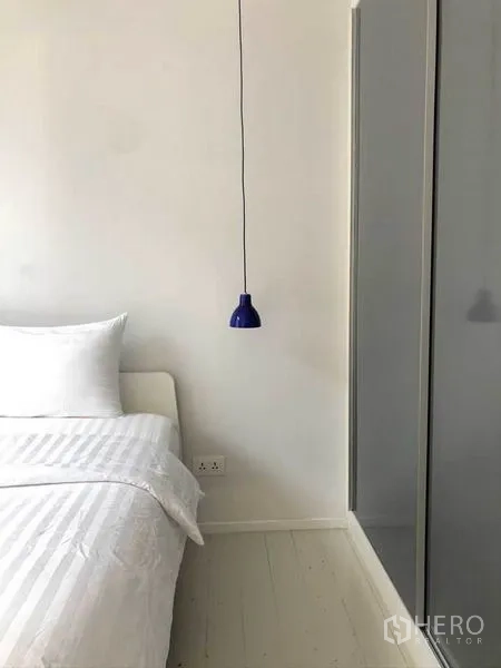 Condominium for sale in Watthana, Bangkok - Cozy bedroom with white bedding, blue pendant light and wardrobe.