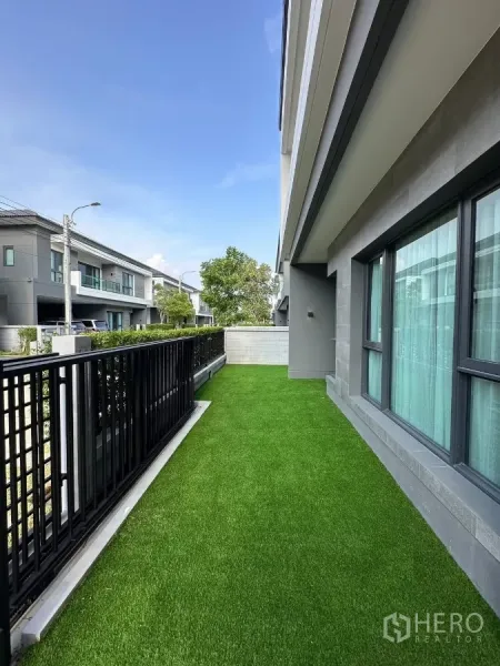 Detached House for rent in Bang Phli, Samut Prakan - Front lawn strip with black metal fence beside large windows of the house.