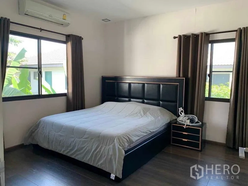 Detached House for rent or sale in Bang Phli, Samut Prakan - Bedroom with upholstered black headboard, bedside tables and two windows with green views.