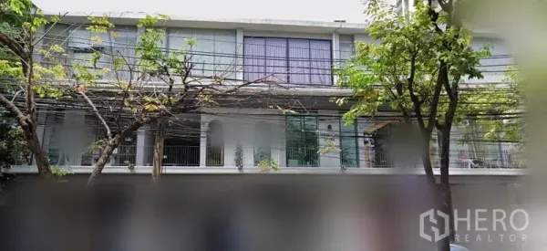 办公空间 出租在Khlong Toei, Bangkok - 低层建筑外观，大幅玻璃窗与阳台护栏，街道行树，位于素坤逸区域。