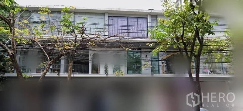 办公空间 出租在Khlong Toei, Bangkok - 低层建筑外观，大幅玻璃窗与阳台护栏，街道行树，位于素坤逸区域。