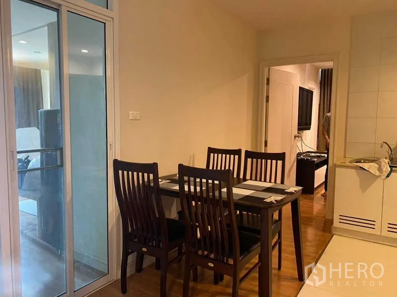 Condominium for rent in Pathum Wan, Bangkok - Cozy dining corner with a four-seat wooden table beside a sliding glass door and kitchenette.