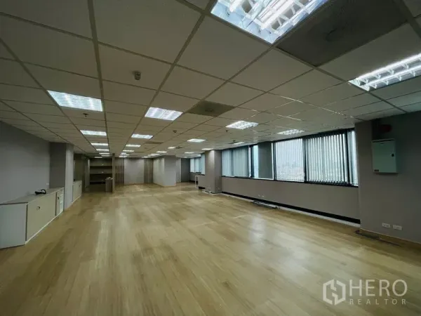 Office Space for rent - Open-plan office with wood flooring, grid ceiling lights and long windows with vertical blinds.