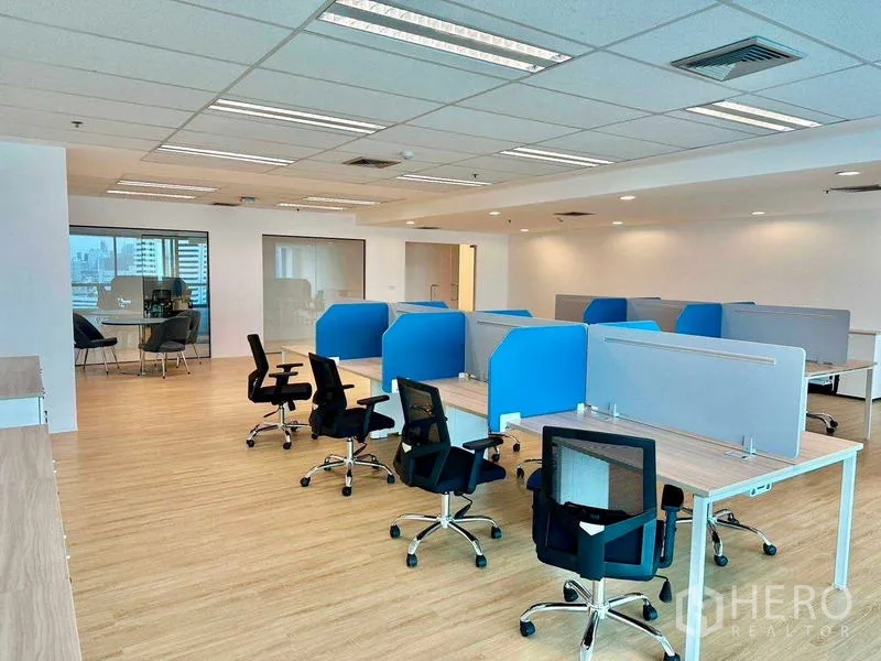 Office Space for rent - Open-plan office with blue-partition workstations, ergonomic chairs, wood flooring, and a glass meeting room.