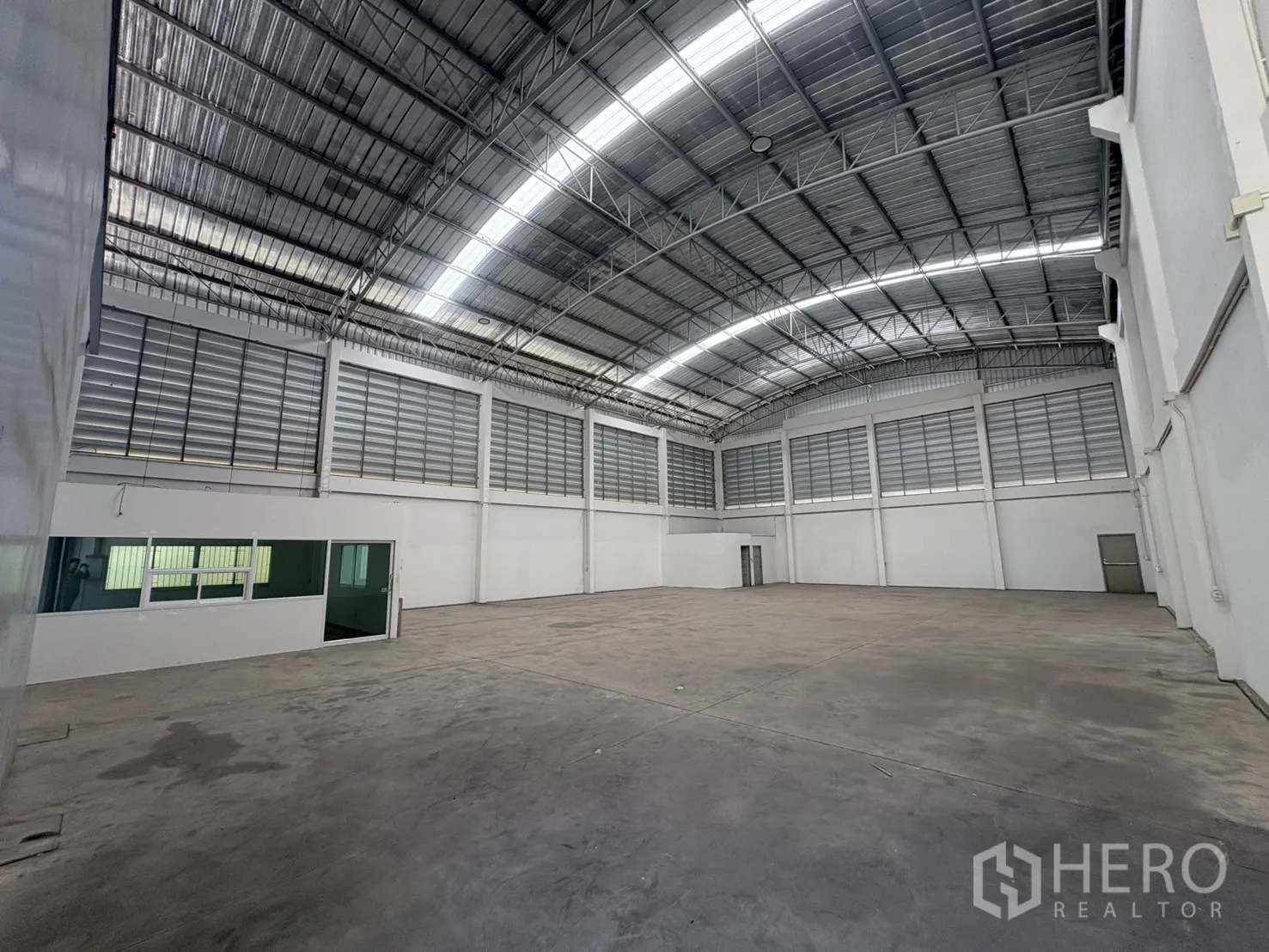 货栈 出租在Ban Phaeo, Samut Sakhon - 仓库内部通透，拱形钢结构屋顶，百叶通风窗与玻璃隔间办公室。