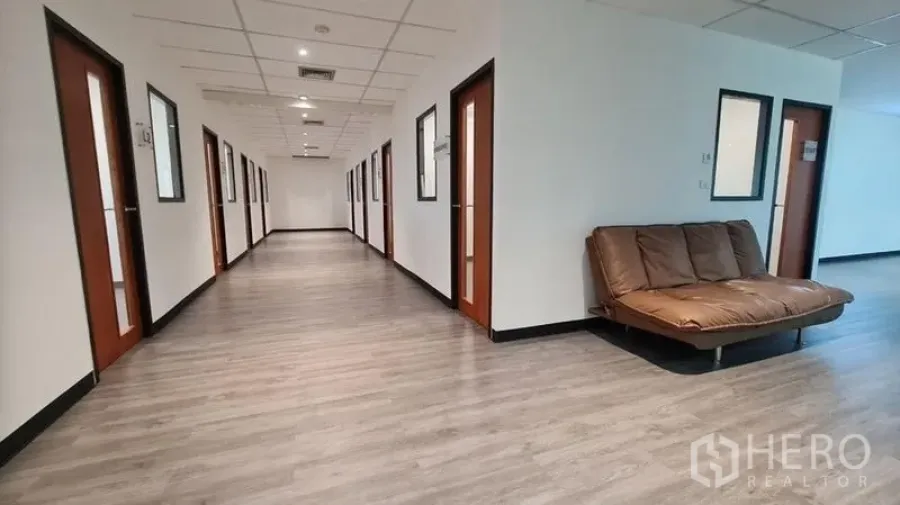 Office Space for rent in Watthana, Bangkok - Wide corridor with private office doors, wood floors and a brown sofa seating area.