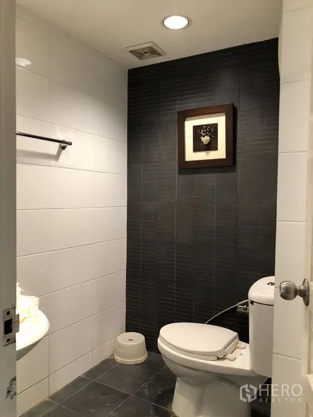 Condominium for rent in Khlong Toei, Bangkok - Guest bathroom with toilet, dark feature wall and tiled floor.