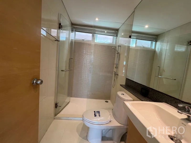Condominium for rent in Watthana, Bangkok - Modern bathroom with glass shower enclosure, toilet and long vanity mirror.