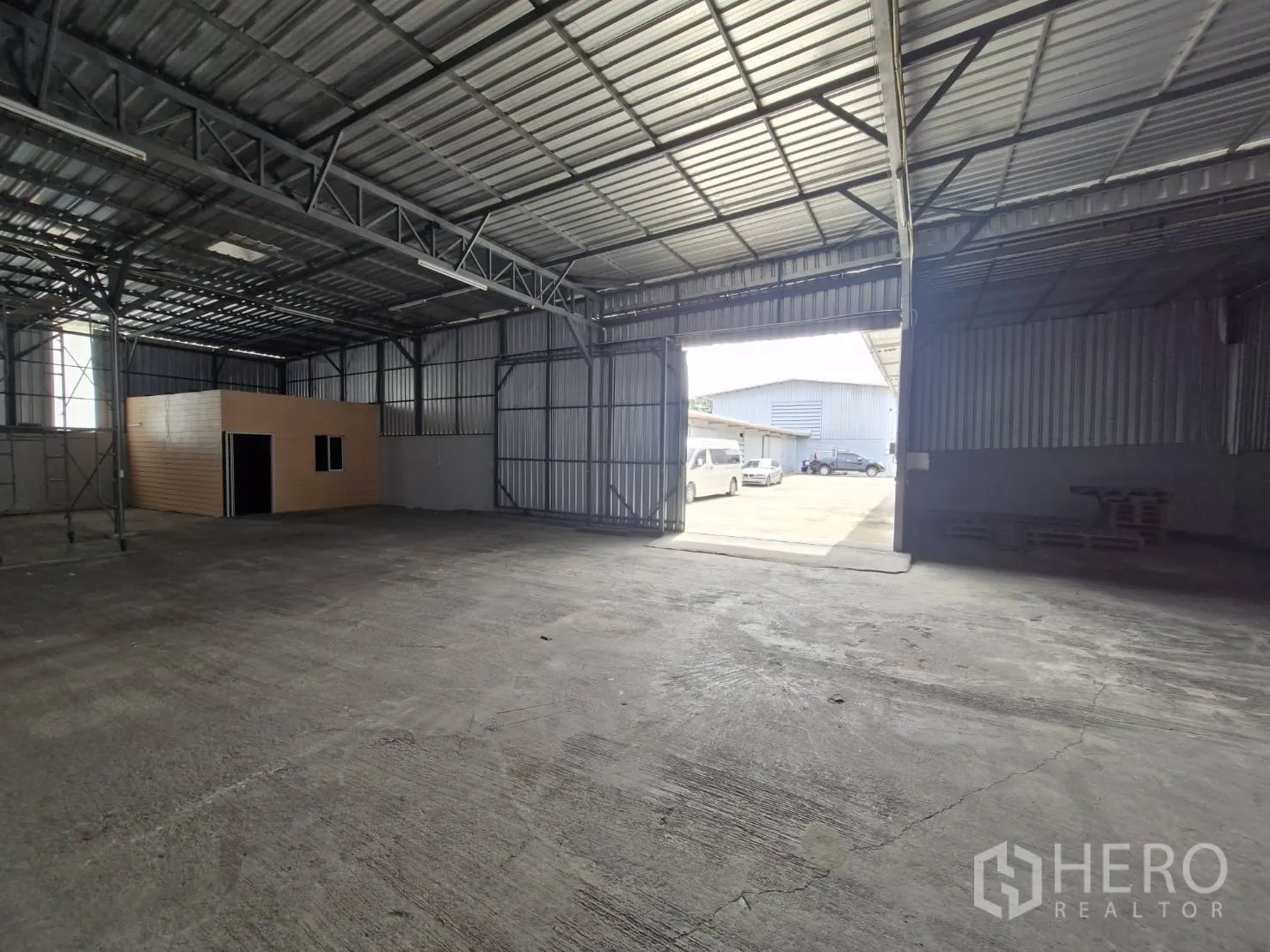 Warehouse for rent in Nakhon Pathom - Interior view toward open doors to the yard, showing an office cabin and vehicle access.