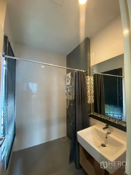 Townhouse for rent or sale in Saphan Sung, Bangkok - Modern bathroom featuring a walk-in shower, vanity sink, large mirror and window blinds.