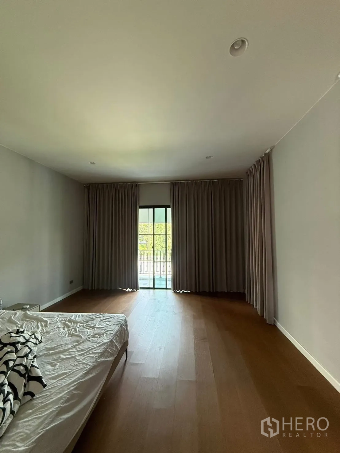 Detached House for rent in Bang Kapi, Bangkok - Master bedroom with floor-to-ceiling curtains, wood flooring and balcony access.