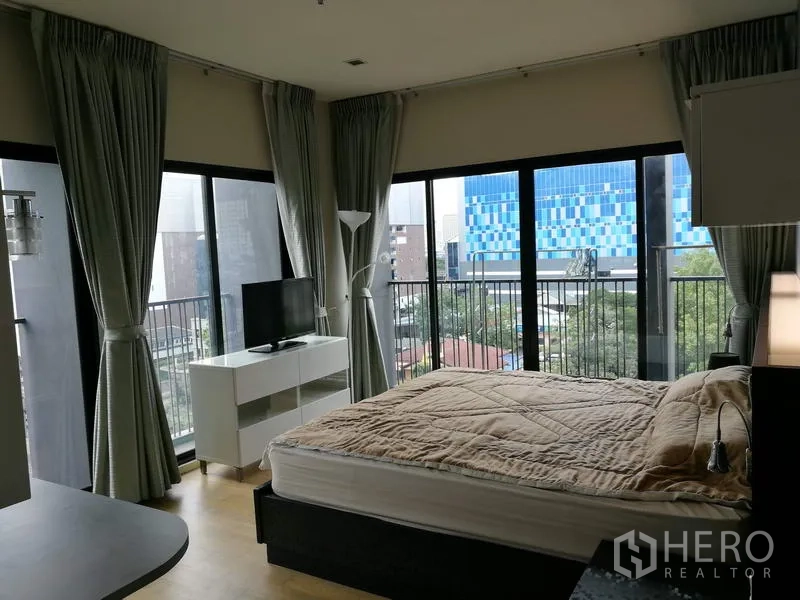 Condominium for rent in Watthana, Bangkok - Corner bedroom with floor-to-ceiling windows, balcony railings, city view, double bed, TV console and grey curtains in an Ekkamai condo.