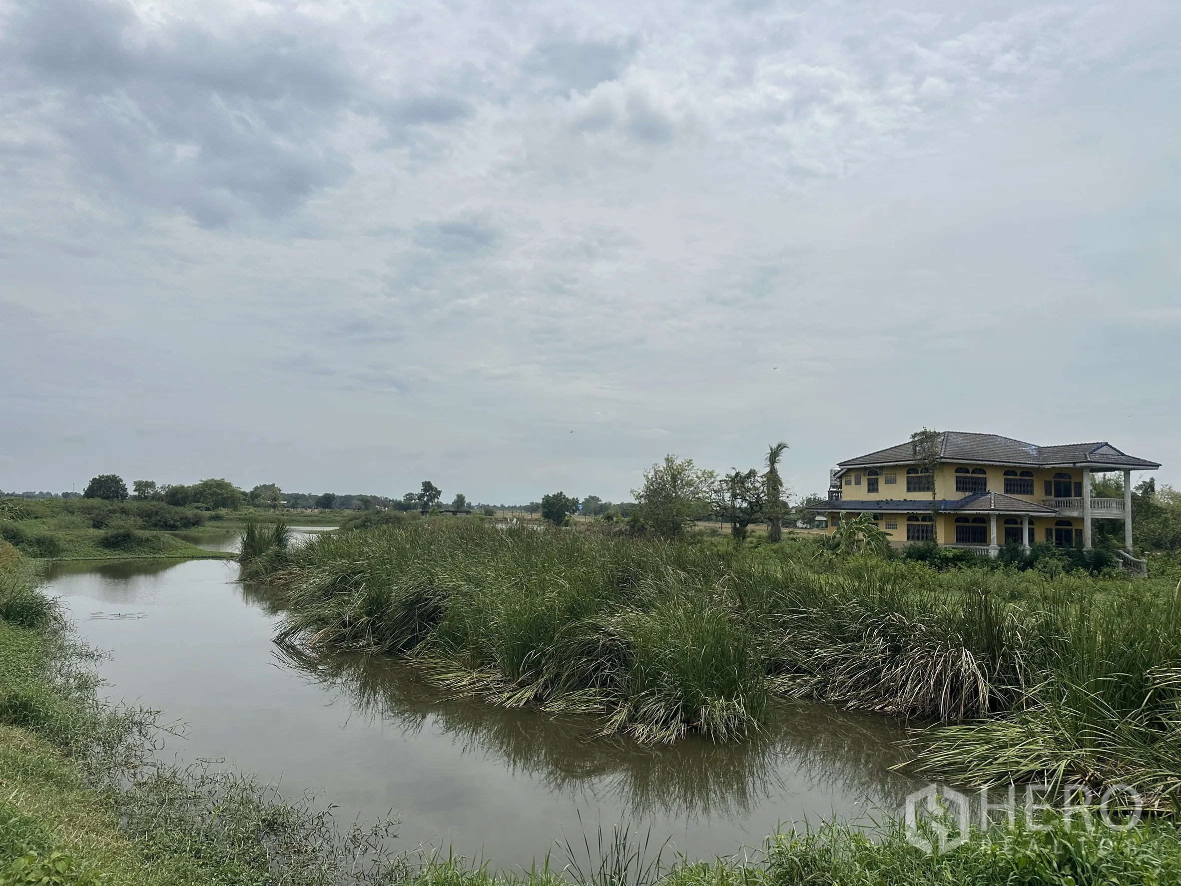 Land for sale in Bang Nam Priao, Chachoengsao - Curving canal bordered by vegetation with a house overlooking the water.
