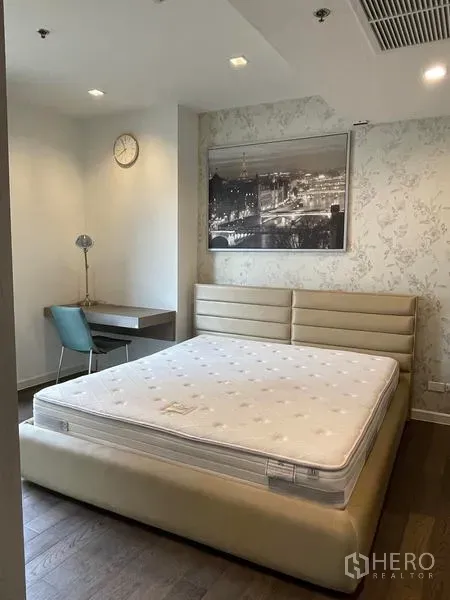 Condominium for rent in Sathon, Bangkok - Spacious master bedroom with upholstered bed frame, desk corner and patterned wallpaper.