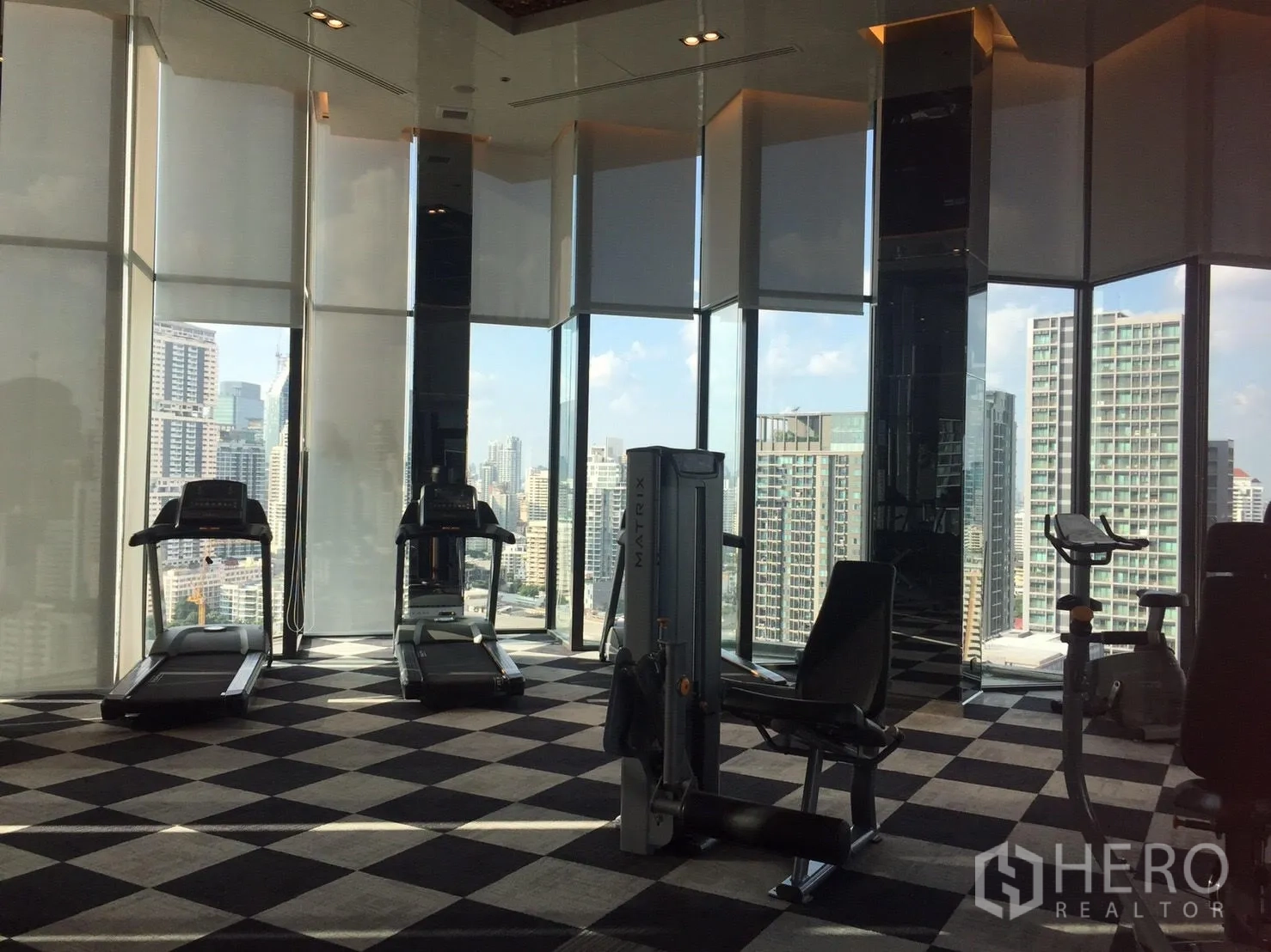 公寓 出租在Khlong Toei, Bangkok - 高空健身房，心肺与力量器械，落地窗面向天际线。