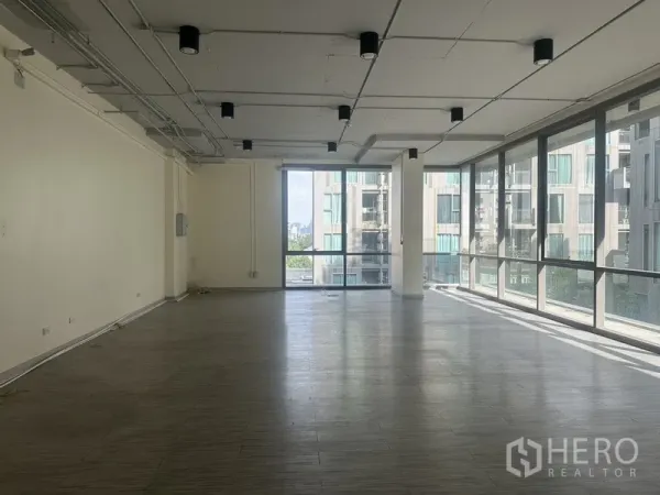 办公空间 出租在Phra Khanong, Bangkok - 明亮的开放式办公室，落地窗与城市景观，木纹地面与外露天花灯。