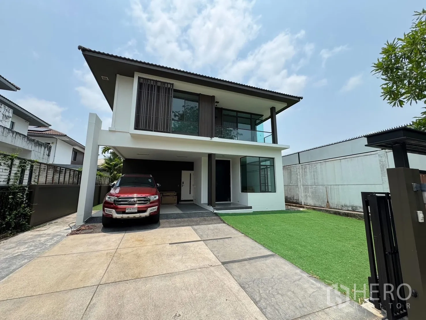 Detached House for rent in Prawet, Bangkok - Front exterior of a two-storey house with covered carport, balcony, driveway and lawn.