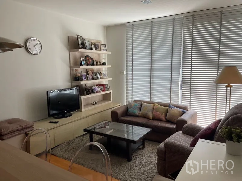 คอนโด ขายในKhlong Toei, Bangkok - มุมห้องนั่งเล่นพร้อมโซฟา ตู้วางทีวี และชั้นโชว์ ติดหน้าต่างสูง