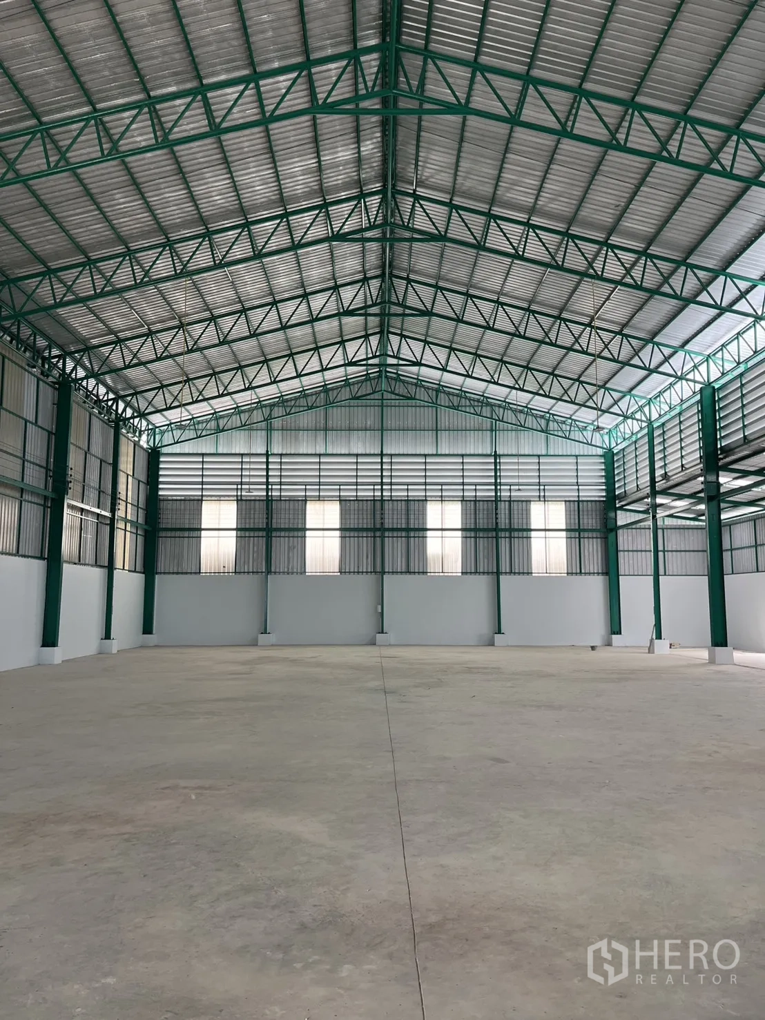 Warehouse for rent in Mueang Samut Sakhon, Samut Sakhon - Warehouse interior with high-clear steel truss roof, natural light panels, ventilation louvers, and a smooth concrete floor.