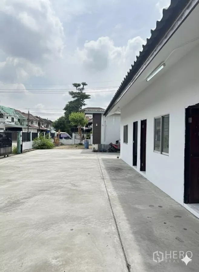 Home Office for rent in Bang Phli, Samut Prakan - Wide driveway and parking apron beside a white single-storey wing with doors and windows.