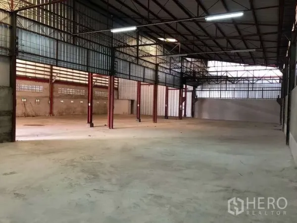 Warehouse for rent in Phra Pradaeng, Samut Prakan - Spacious warehouse interior with high steel‑truss roof, red columns and smooth concrete floor with natural light panels.