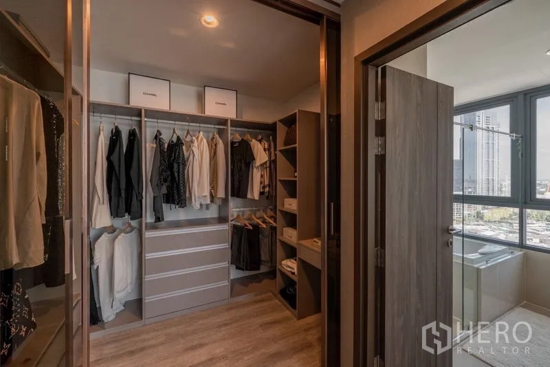 Condominium for rent in Bang Na, Bangkok - Walk-in closet with custom cabinetry and shelving, next to a bright window and bathroom.