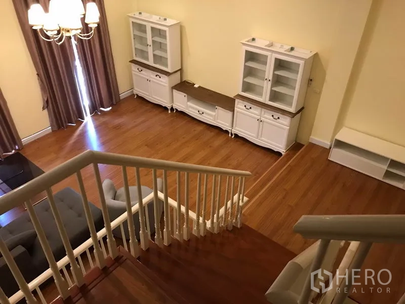 Townhouse for rent in Wang Thonglang, Bangkok - View from the staircase over the living room with chandelier, wood flooring and classic white storage units.